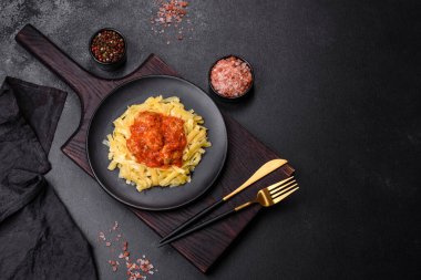Köfteli spagetti siyah bir kasede domates sosu ile koyu beton arka planda.