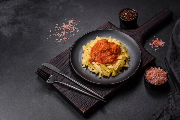 Köfteli spagetti siyah bir kasede domates sosu ile koyu beton arka planda.