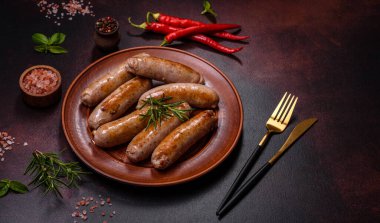 Baharatlı ızgara sosis ve koyu beton arka planda tuz ve biberli otlar. Açık ateşte pişmiş et yemeği.