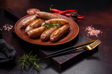 Baharatlı ızgara sosis ve koyu beton arka planda tuz ve biberli otlar. Açık ateşte pişmiş et yemeği.