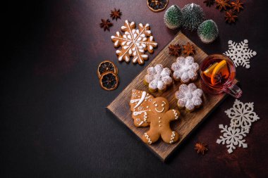 Bir dilim portakallı sıcak şarap, tarçın, karanfil ve diğer baharatlarla çikolatalı kekler ve koyu beton arka planda Noel süslemeleri.