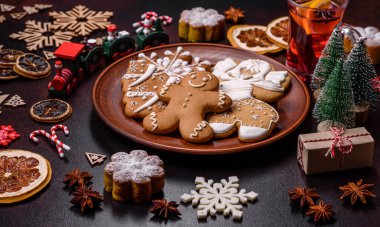 Bir dilim portakallı sıcak şarap, tarçın, karanfil ve diğer baharatlarla çikolatalı kekler ve koyu beton arka planda Noel süslemeleri.