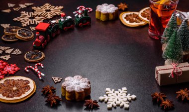 Bir dilim portakallı sıcak şarap, tarçın, karanfil ve diğer baharatlarla çikolatalı kekler ve koyu beton arka planda Noel süslemeleri.