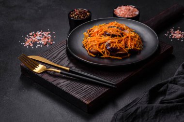 Sarımsaklı, siyah desenli bir tabakta havuçlu Kore salatası ve patlıcan.