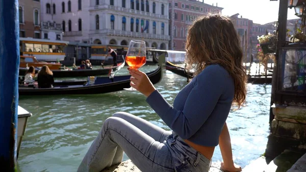 Kız el ele tutuşup aşk şehrinde bir bardak Spritz içiyor - aperatif, alkollü içecek Spritz Camapari ya da Aperol - Venedik 'in tipik içeceği beyaz şaraptan, portakallı - Rialto Köprüsü 