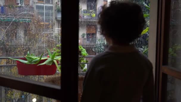 ヨーロッパ イタリア ミラノ 彼の家のバルコニーから雪 クリスマスの街の降雪 コロナウイルスCovid 19流行のために封鎖中に7歳の男の子 Omicronバリアント — ストック動画