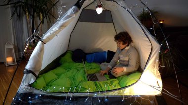 Çocuk 7 yaşında, Covid-19 Coronavirus tecridi sırasında bir çadırda dizüstü bilgisayar izliyor. Salgın sırasında apartmanda akıllı çalışma ve yaşam tarzı.