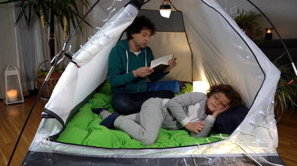 İtalya, Milano - Baba oğul uyutur ve Covid-19 Coronavirus salgını sırasında evdeki çadırda bir masal okur - aile babası ve oğlunun yaşam tarzı - seyahat etme arzusu