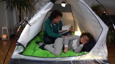 İtalya, Milano - Baba oğul uyutur ve Covid-19 Coronavirus salgını sırasında evdeki çadırda bir masal okur - aile babası ve oğlunun yaşam tarzı - seyahat etme arzusu