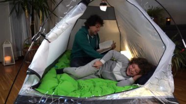 İtalya, Milano - Baba oğul uyutur ve Covid-19 Coronavirus salgını sırasında evdeki çadırda bir masal okur - aile babası ve oğlunun yaşam tarzı - seyahat etme arzusu