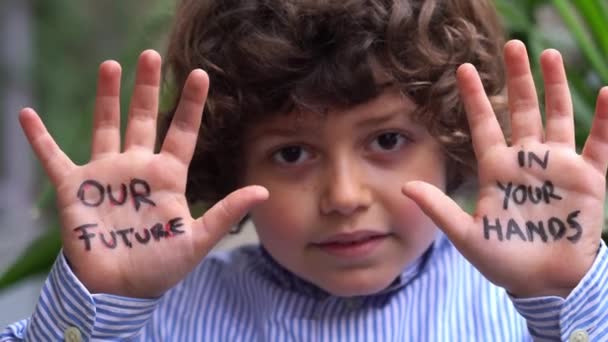 7歳の男の子が手を上げて手のひらに私たちの未来に碑文 地球を救え 私たちの世界はあなたの手にあります 世界を救うためのコンセプトデザイン 持続可能な環境 気候変動は地球の未来です — ストック動画