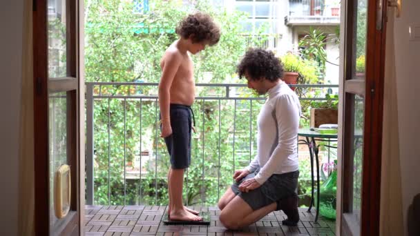 父と7歳の息子の少年は スポーツ活動後にバルコニーで体重を測定します 春の到着と物理的なトレーニング彼らは夏の準備を取得します — ストック動画