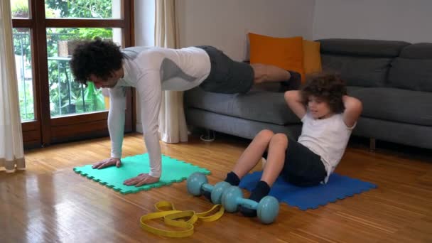 随着春天的到来 父亲和7岁的儿子在家里做体操 他们准备迎接夏天的到来 做俯卧撑 做室内体育活动 — 图库视频影像