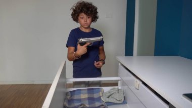 An 8-year-old boy alone at home finds a real gun in his parents' drawer - in America more and more children find guns in domestic places - social danger and violence