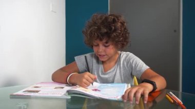 footage  of 8-year-old boy child does elementary school homework for summer at home during holidays - writing on textbook during Covid-19 Coronavirus epidemic lockdown outbreak