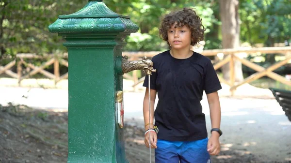8-year-old child drinks and refreshes himself with water from the fountain - record heat hot day  in summer with temperatures over 40 degrees - Global warming and climate Change in Milan