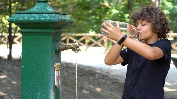 8-year-old child drinks and refreshes himself with water from the fountain - record heat hot day  in summer with temperatures over 40 degrees - Global warming and climate Change in Milan