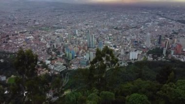 Güney Amerika 'nın Bogota şehrinin başkenti Kolombiya' nın insansız hava aracı görüntüsü - Cerro Monserrate 'den görülen yeşil ağaçların arasına gömülü modern silueti olan büyük megalopolis