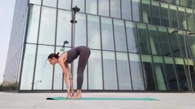 21 yaşındaki kız, modern şehir merkezindeki gökdelenlerin yakınında yoga jimnastik yapıyor. Milano şehrinde rahatlama ve meditasyon. Şehir hayatının koşuşturması ve çabasıyla fiziksel ve zihinsel egzersizlerle mücadele ediyor.