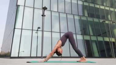 21 yaşındaki kız, modern şehir merkezindeki gökdelenlerin yakınında yoga jimnastik yapıyor. Milano şehrinde rahatlama ve meditasyon. Şehir hayatının koşuşturması ve çabasıyla fiziksel ve zihinsel egzersizlerle mücadele ediyor.