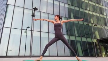 21 yaşındaki kız, modern şehir merkezindeki gökdelenlerin yakınında yoga jimnastik yapıyor. Milano şehrinde rahatlama ve meditasyon. Şehir hayatının koşuşturması ve çabasıyla fiziksel ve zihinsel egzersizlerle mücadele ediyor.