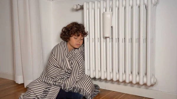 increase in the cost of gas and heating problems in homes due to the energy crisis - a boy at home near the heater to heat suffers from the cold