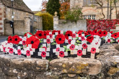 A close up view of the wooden crosses with paper poppies and knitted poppies displayed on remembrance day in the flower bed to one side of the war memorial in Melksham, Wiltshire