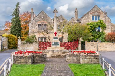 The war memorial in the Wiltshire town of Melksham on remembrance day. A net of knitted poppies is draped on a garden wall forming a backdrop and the flower beds either side are filled with small crosses and knitted poppies.