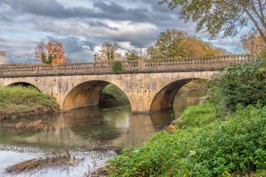 A view of the Melksham Town Bridge looking up river on an autumn day. The bridge on Bath Road crosses the River Avon and is a grade 2 listed structure of ashlar with arches and a balustraded parapet