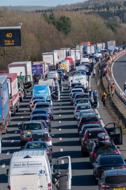 3 lanes of queued traffic on a British motorway with drivers out of their cars when a traffic jam forms due to motorway closure because of an emergency incident