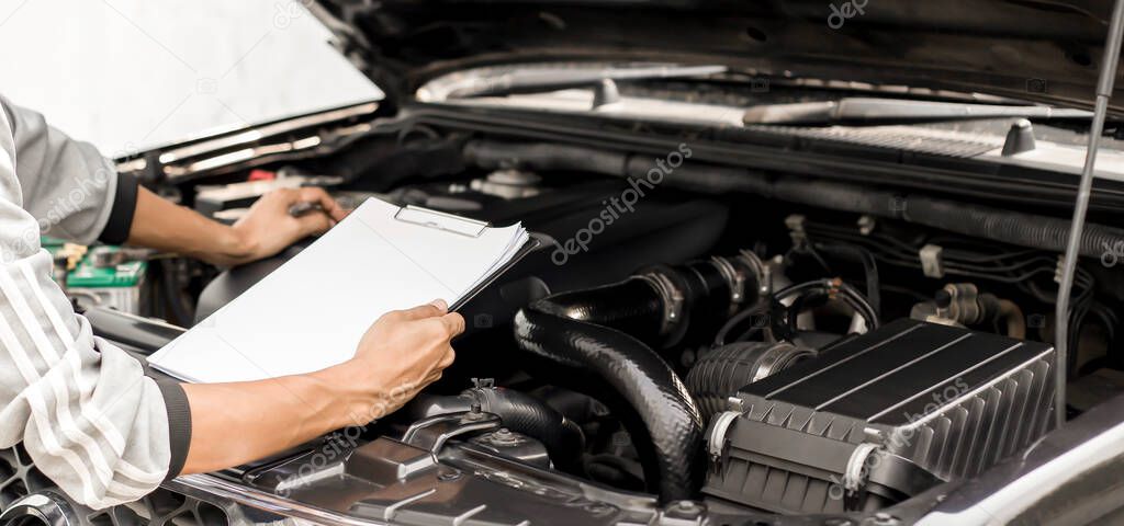 Automobile mechanic repairman checking a car engine with inspecting writing to the clipboard the checklist for repair machine, car service and maintenance.