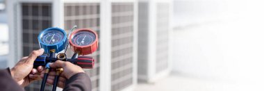 Hava onarım teknisyeni endüstriyel fabrika klimalarını doldurmak ve dış hava kompresörü ünitesini kontrol etmek için ölçüm ekipmanı kullanıyor..