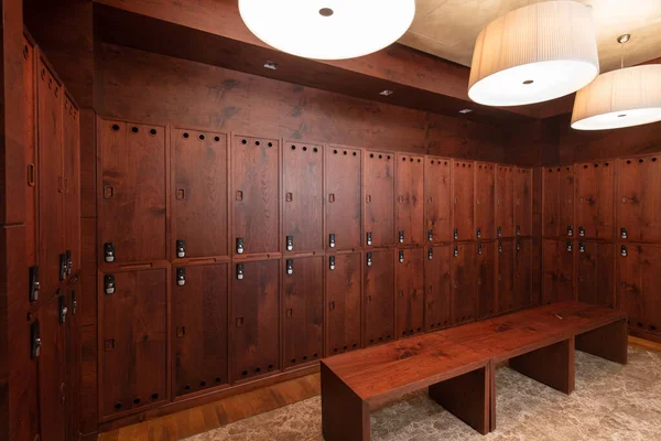 Interior of a locker room. Clean empty dressing room with big lockers with wooden door and wooden bench