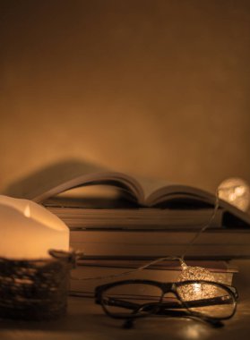 un libro aperto in cima ad altri libri in colonna con una candela che illumina