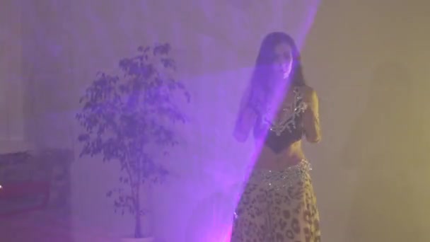 Silhouette einer Frau in einem exotischen Kostüm, die einen Bauchtanz aufführt und ihren halbnackten Körper bewegt. Gedreht in einem dunklen Studio mit Rauch und gelbem Neonlicht.