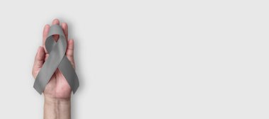 Beyin kanseri ve tümör farkındalığı, alerji, astım kontrolü ve diyabet önleme için gri ya da gri kurdele. Beyaz arka planda el üstünde eğilin