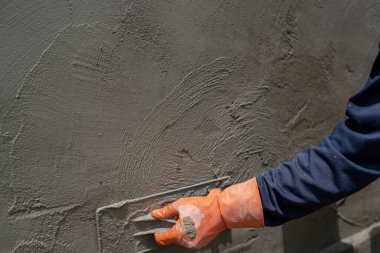 Close-up shot of a cement worker using a trowel to plaster cement in construction.