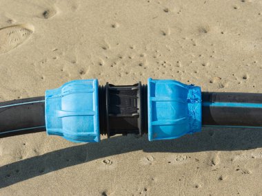 İki polietilen boruyu birleştirmek için kullanılan mekanik sıkıştırma plastiği. Arka planda Kum Gölgesi