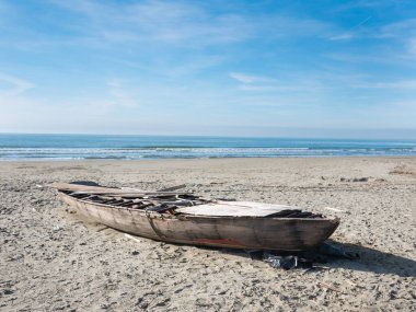 hull of a shipwrecked small sailboat on the beach. It is possible to see the rough wooden structure