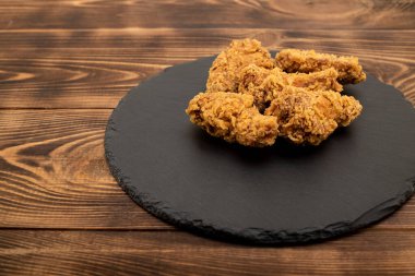 Baharatlı, bol yağda kızartılmış tavuk kanatları. Ahşap bir arka planda siyah bir tabakta.