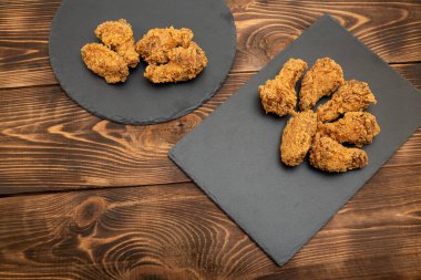 Baharatlı, bol yağda kızartılmış tavuk kanatları. Ahşap bir arka planda siyah bir tabakta.