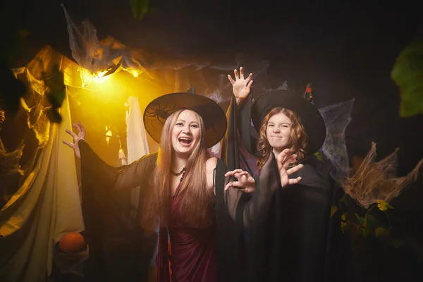 Two young women looking like witches are having fun on Halloween in a dark room with yellow light and smoke. Carnival concept and Halloween party