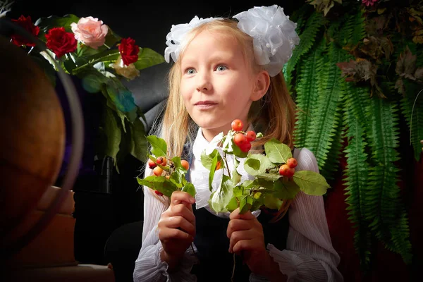 Girl who is elementary school children in uniform having photo shoot in school holiday on September 1 on black background with flowers. Holiday of beginning of school and studing in Russia