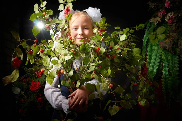 Girl who is elementary school children in uniform having photo shoot in school holiday on September 1 on black background with flowers. Holiday of beginning of school and studing in Russia