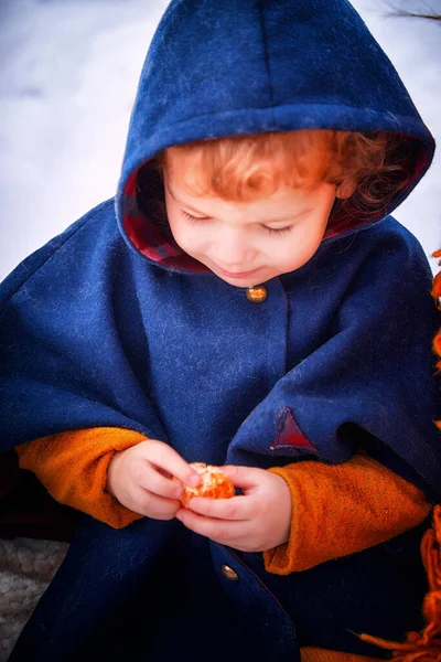 Beautiful young girl dressed in blue coat holds tangerine or orange in her hands, eats and smiles. Orange fruits, she bites an orange and she likes