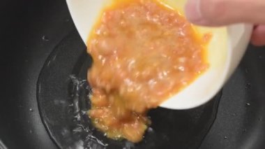 Kızarmış Tayland omleti ve elektrikli tavada sıcak yağ pişirmek için fincandan domuz eti dökülüyor.