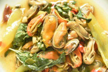 Baharatlı kızarmış midye dilimlenmiş soğan ve tabakta fesleğen yaprağı.