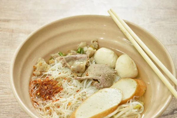 vermicelli rice noodles topping chop boiled pork and fish ball in soup dressing cayenne pepper on bowl