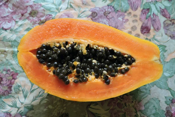 半分に切ったジューシーなオレンジ色のパパイヤの果実 黒い種子 花の背景 — ストック写真