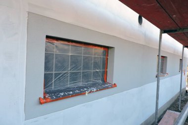 Üstü asal ve kısmen kaplanmış bir dış duvar, bir cam blok pencere ve koruyucu bir filmle kaplı bir pencere pervazı